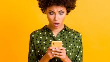Photo of a woman looking at her phone with a shocked expression to illustrate the article How to Stop Doomscrolling